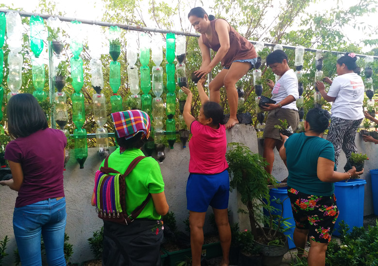 woman climbing up a wall while other women support her to install plants in verticl garden